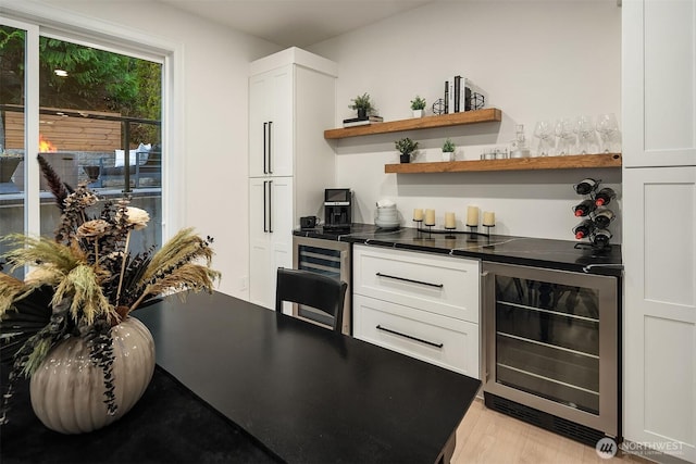 kitchen with dark countertops, light wood-style flooring, wine cooler, and white cabinets