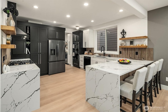 kitchen featuring open shelves, a sink, light stone countertops, stainless steel fridge, and a peninsula