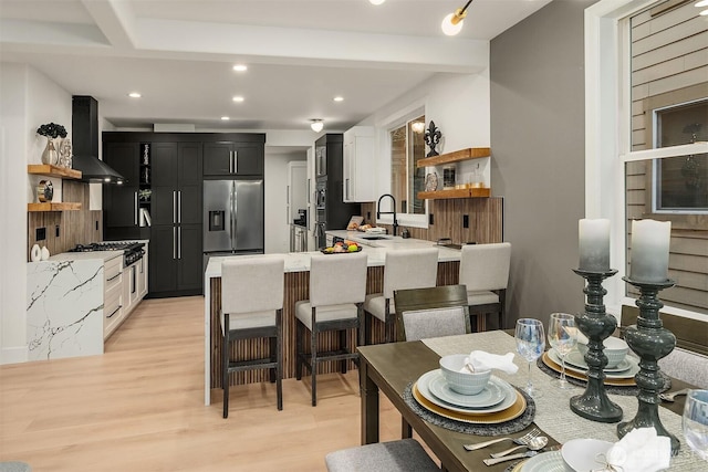 kitchen featuring a peninsula, wall chimney range hood, open shelves, a sink, and built in fridge