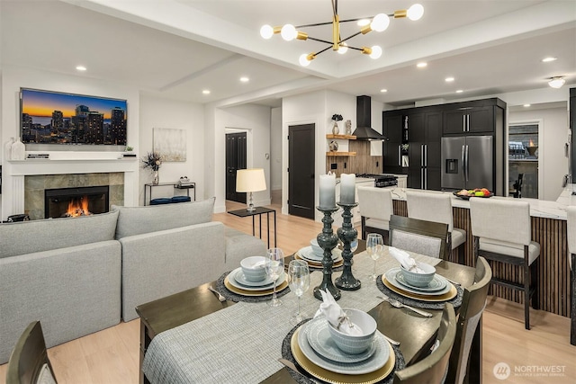 dining space featuring a notable chandelier, light wood-style flooring, beam ceiling, and a tile fireplace