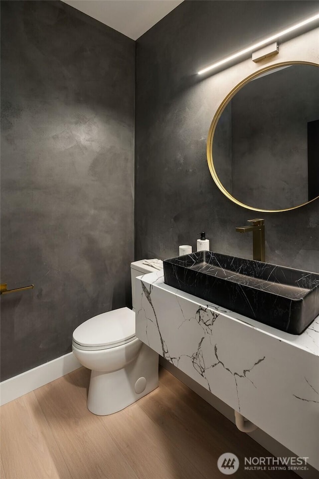 half bath featuring a sink, toilet, and wood finished floors