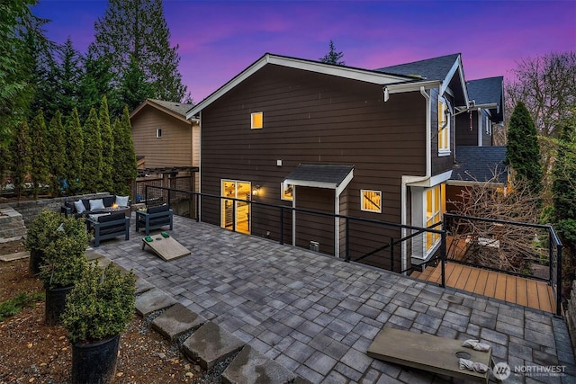 back of property at dusk featuring a patio area, an outdoor living space, and roof with shingles