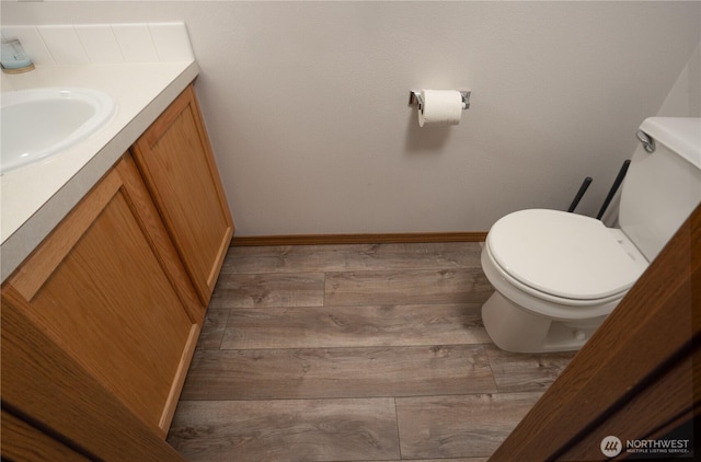 half bath with toilet, vanity, baseboards, and wood finished floors