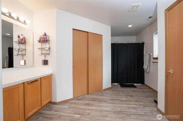 full bath with a shower with shower curtain, vanity, wood finished floors, baseboards, and visible vents