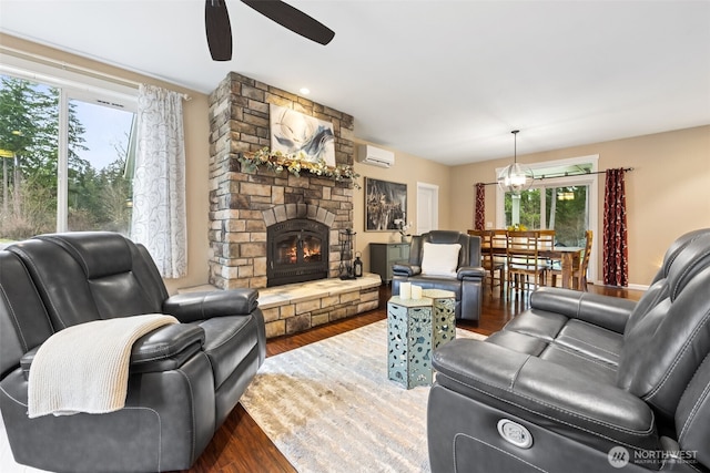 living room with a wall unit AC, ceiling fan, a stone fireplace, and wood finished floors