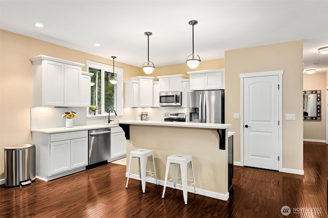 kitchen featuring stainless steel appliances, dark wood-style flooring, light countertops, decorative backsplash, and a kitchen bar