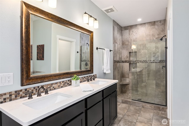 bathroom featuring tasteful backsplash, tiled shower, a sink, and visible vents