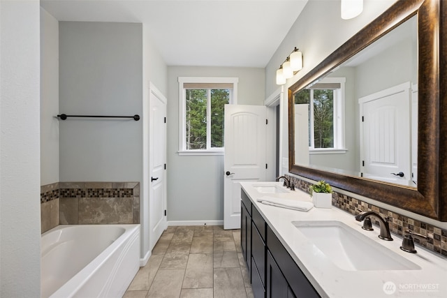 full bathroom featuring double vanity, a sink, a bath, and baseboards