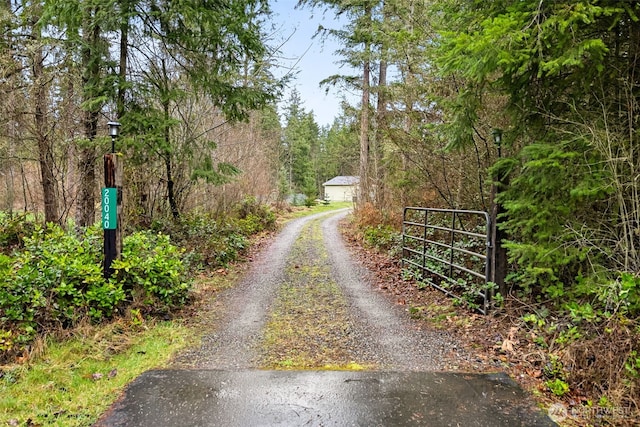 view of road with driveway, a gated entry, and a view of trees