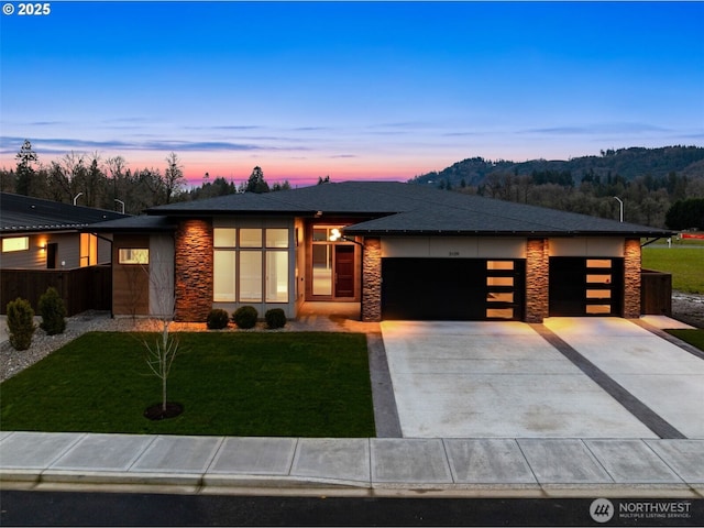 prairie-style house with driveway, stone siding, a garage, and a yard