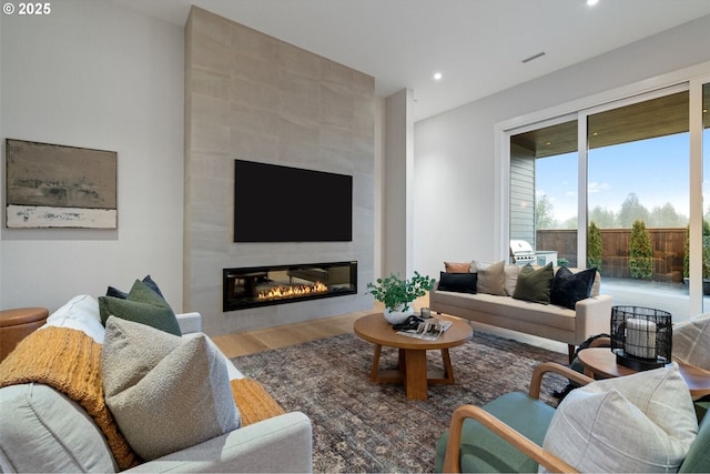 living room with a tile fireplace, visible vents, recessed lighting, and wood finished floors