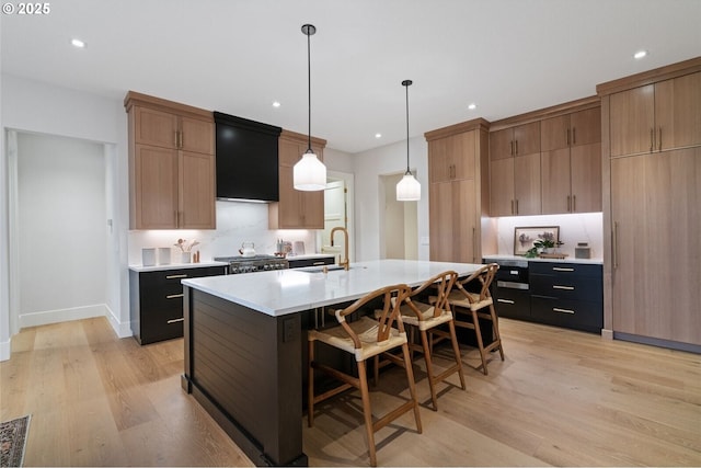 kitchen with a center island with sink, decorative backsplash, light countertops, light wood-style floors, and a sink