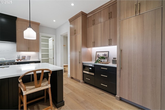 kitchen with light wood finished floors, stainless steel microwave, gas range oven, light countertops, and pendant lighting