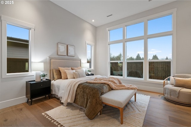 bedroom featuring recessed lighting, visible vents, a towering ceiling, wood finished floors, and baseboards