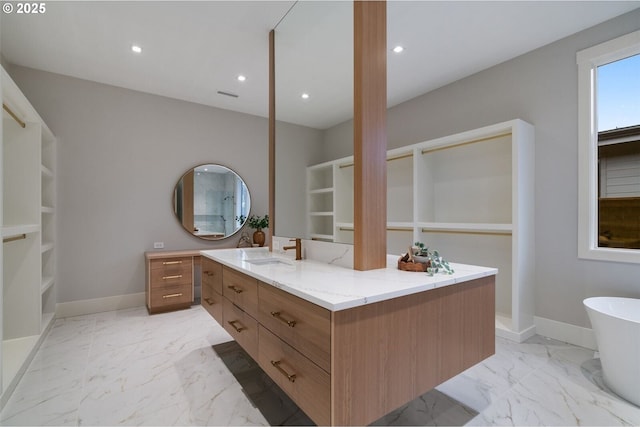 bathroom featuring marble finish floor, baseboards, a freestanding bath, and vanity