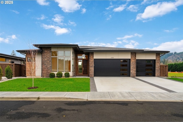 prairie-style house with fence, a garage, stone siding, driveway, and a front lawn