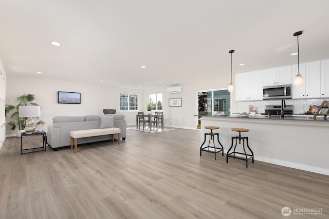 living room featuring recessed lighting, an AC wall unit, baseboards, and light wood finished floors