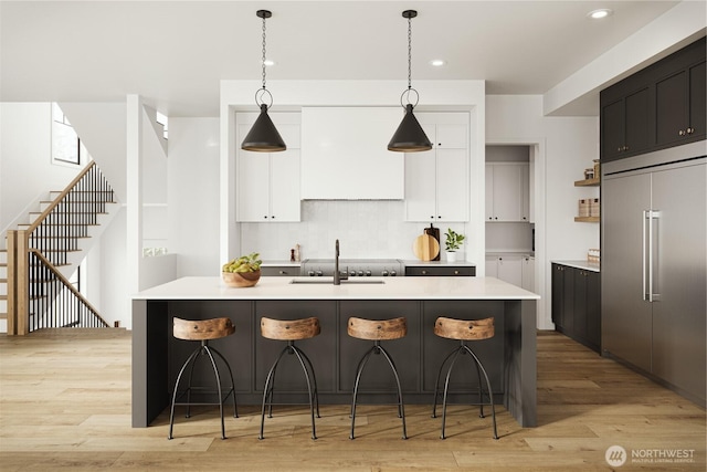 kitchen featuring light countertops, white cabinetry, a sink, light wood-type flooring, and built in refrigerator