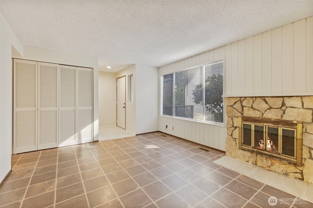 unfurnished living room with a fireplace, visible vents, a textured ceiling, and tile patterned floors