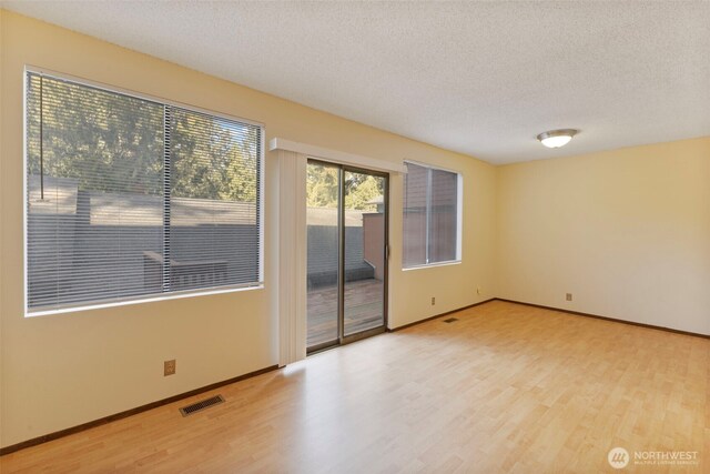 spare room with visible vents, a textured ceiling, baseboards, and wood finished floors