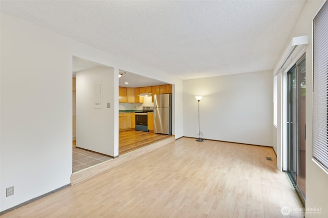 unfurnished living room with light wood-type flooring, baseboards, visible vents, and a textured ceiling