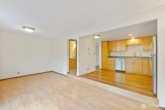 kitchen featuring a textured ceiling, light brown cabinets, baseboards, light wood-style floors, and appliances with stainless steel finishes