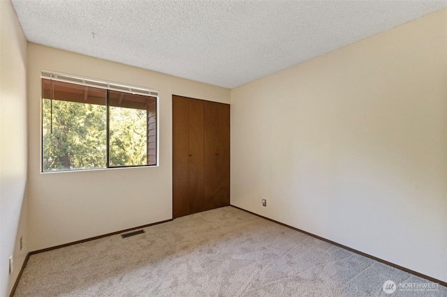 unfurnished bedroom with carpet, visible vents, a textured ceiling, and baseboards