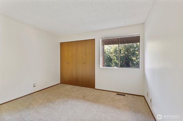 unfurnished bedroom with baseboards, visible vents, a textured ceiling, carpet floors, and a closet