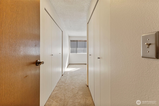 corridor with a textured wall, a textured ceiling, and light colored carpet