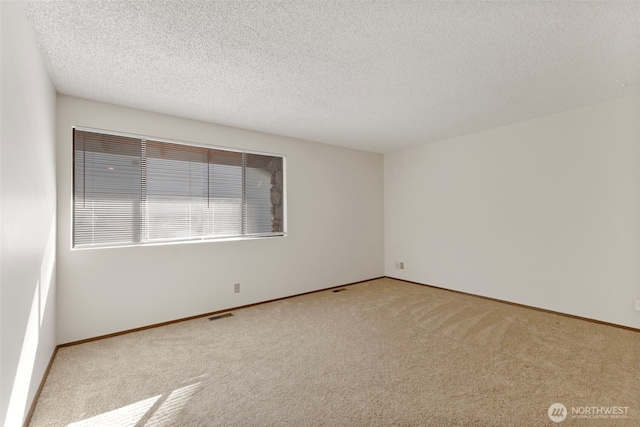 carpeted empty room with baseboards, visible vents, and a textured ceiling