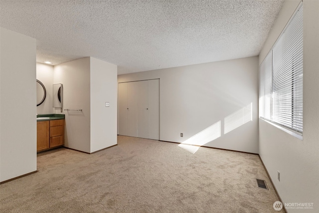 interior space with light carpet, baseboards, visible vents, and a textured ceiling