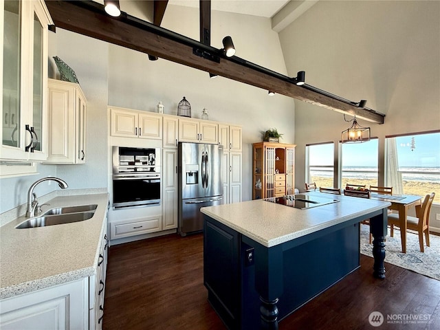 kitchen with a sink, beamed ceiling, appliances with stainless steel finishes, high vaulted ceiling, and a kitchen island with sink