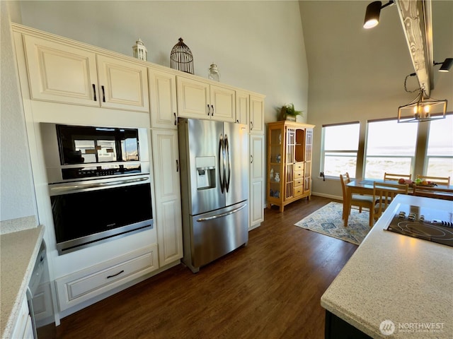 kitchen featuring dark wood-type flooring, black appliances, cream cabinets, light stone countertops, and a towering ceiling