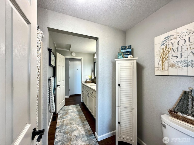 bathroom with vanity, toilet, wood finished floors, and a textured wall