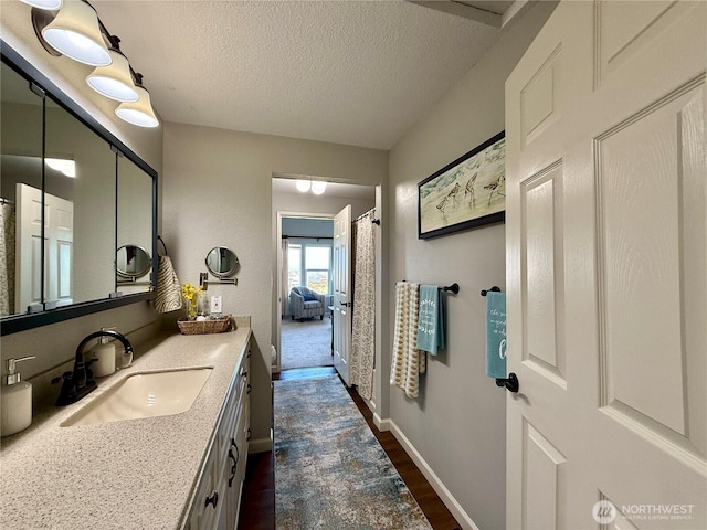 full bath with a textured ceiling, vanity, baseboards, and wood finished floors