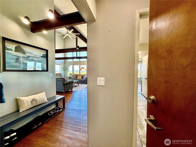 corridor with vaulted ceiling with beams, wood finished floors, and a textured wall