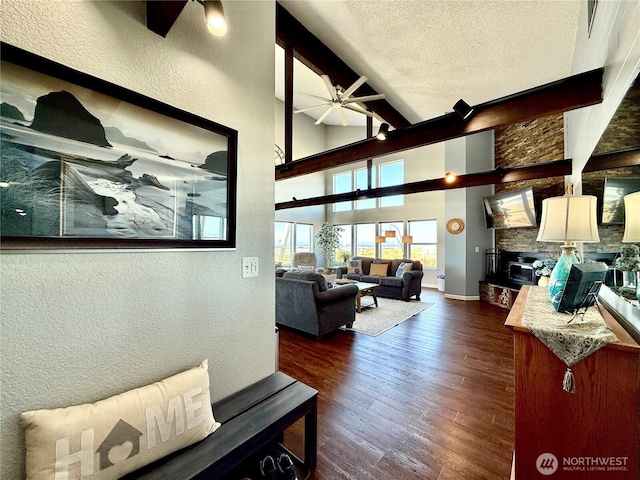 living room featuring baseboards, ceiling fan, dark wood-type flooring, a textured ceiling, and beamed ceiling