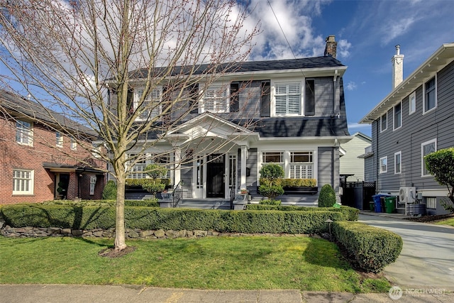 view of front of house featuring a chimney, a front lawn, and a shingled roof