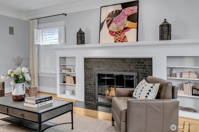 living room with visible vents, built in shelves, ornamental molding, wood finished floors, and a glass covered fireplace