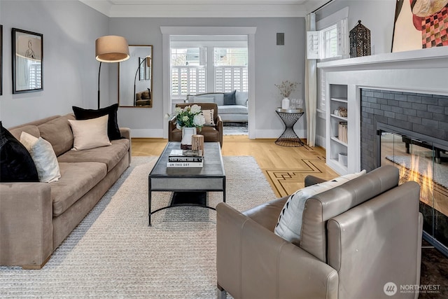 living room with a glass covered fireplace, wood finished floors, baseboards, and ornamental molding