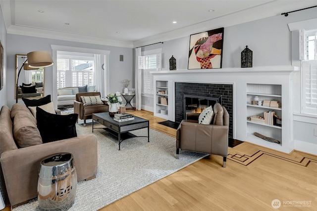 living room featuring built in shelves, crown molding, recessed lighting, a fireplace, and wood finished floors