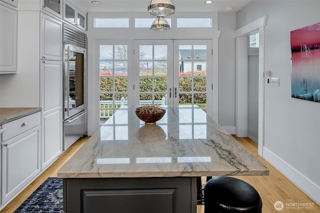 kitchen featuring white cabinetry, light wood-style flooring, light stone countertops, and a center island