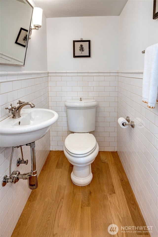 half bath with tile walls, toilet, wood finished floors, and wainscoting