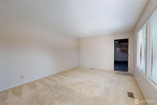 spare room with light carpet, visible vents, and a textured ceiling