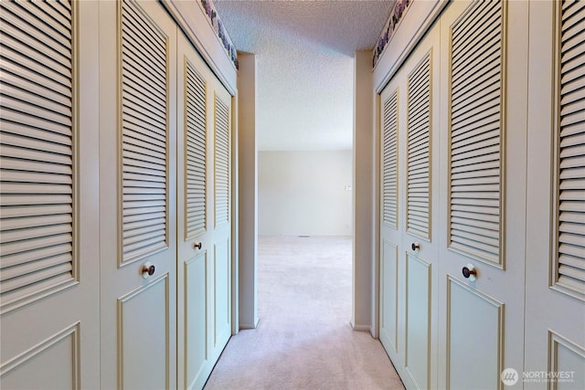 hall featuring a textured ceiling and light colored carpet