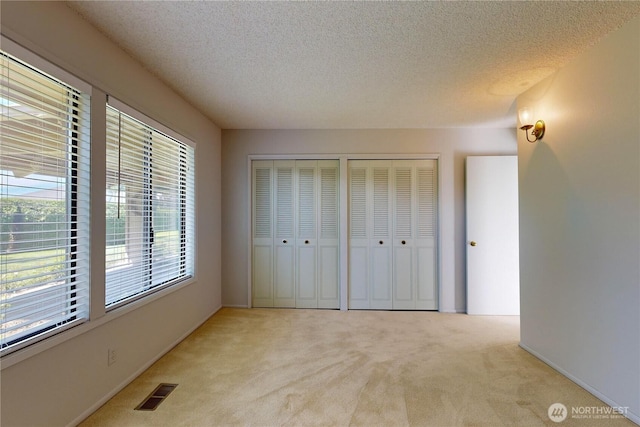 unfurnished bedroom featuring multiple closets, visible vents, light carpet, and a textured ceiling