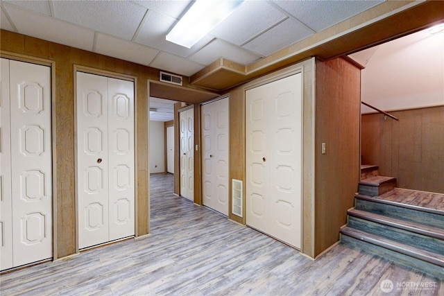 finished basement with a paneled ceiling, wooden walls, wood finished floors, visible vents, and stairs