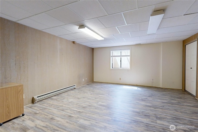 empty room with wooden walls, baseboard heating, and wood finished floors