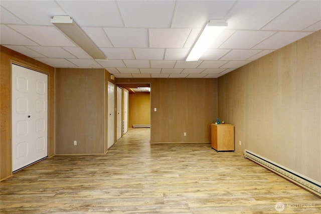 spare room with light wood finished floors, a baseboard radiator, wooden walls, and baseboard heating