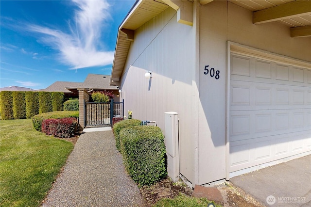 property entrance with an attached garage, fence, a lawn, a gate, and stucco siding